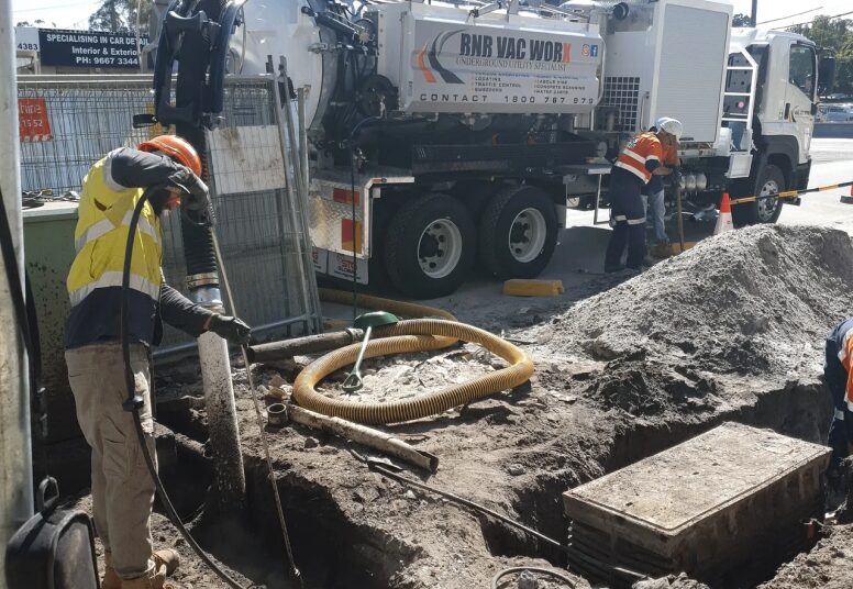Workers using vacuum excavation equipment at construction site.
